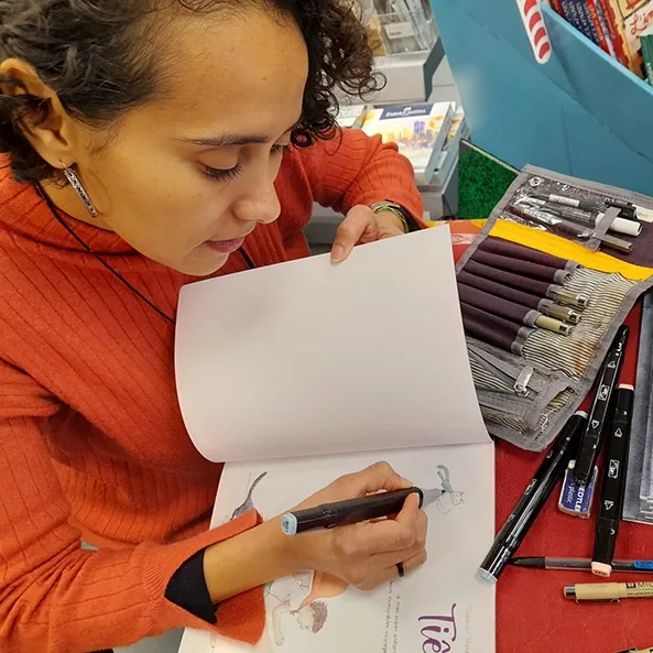 Débora Borba dédicace un exemplaire de Tiê, sa trousse de feutres ouverte sur la table